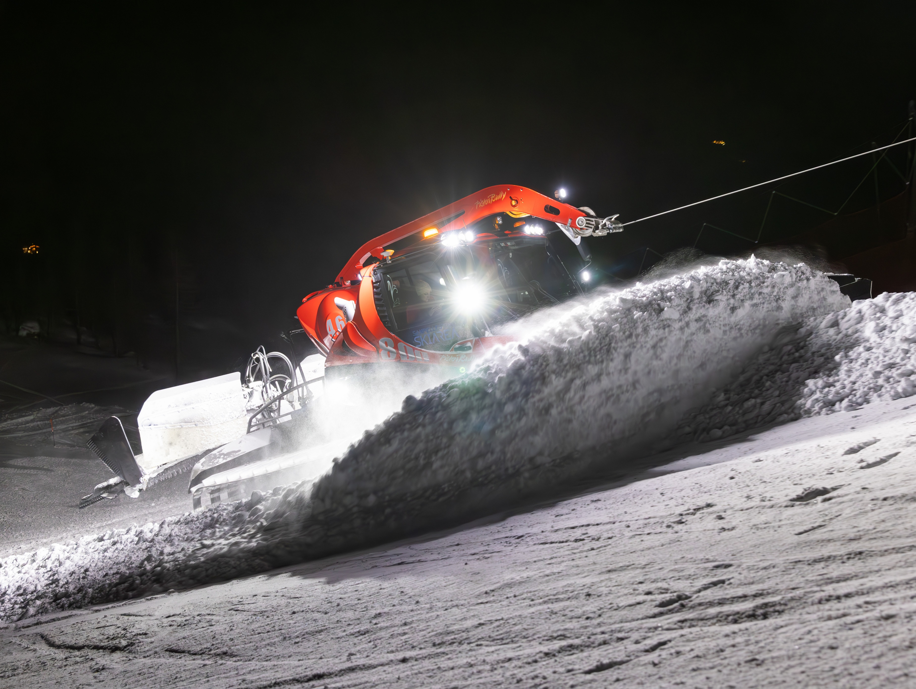 Pistenraupe schiebt bei Nacht im Scheinwerferlicht Schnee einen Hang hinauf