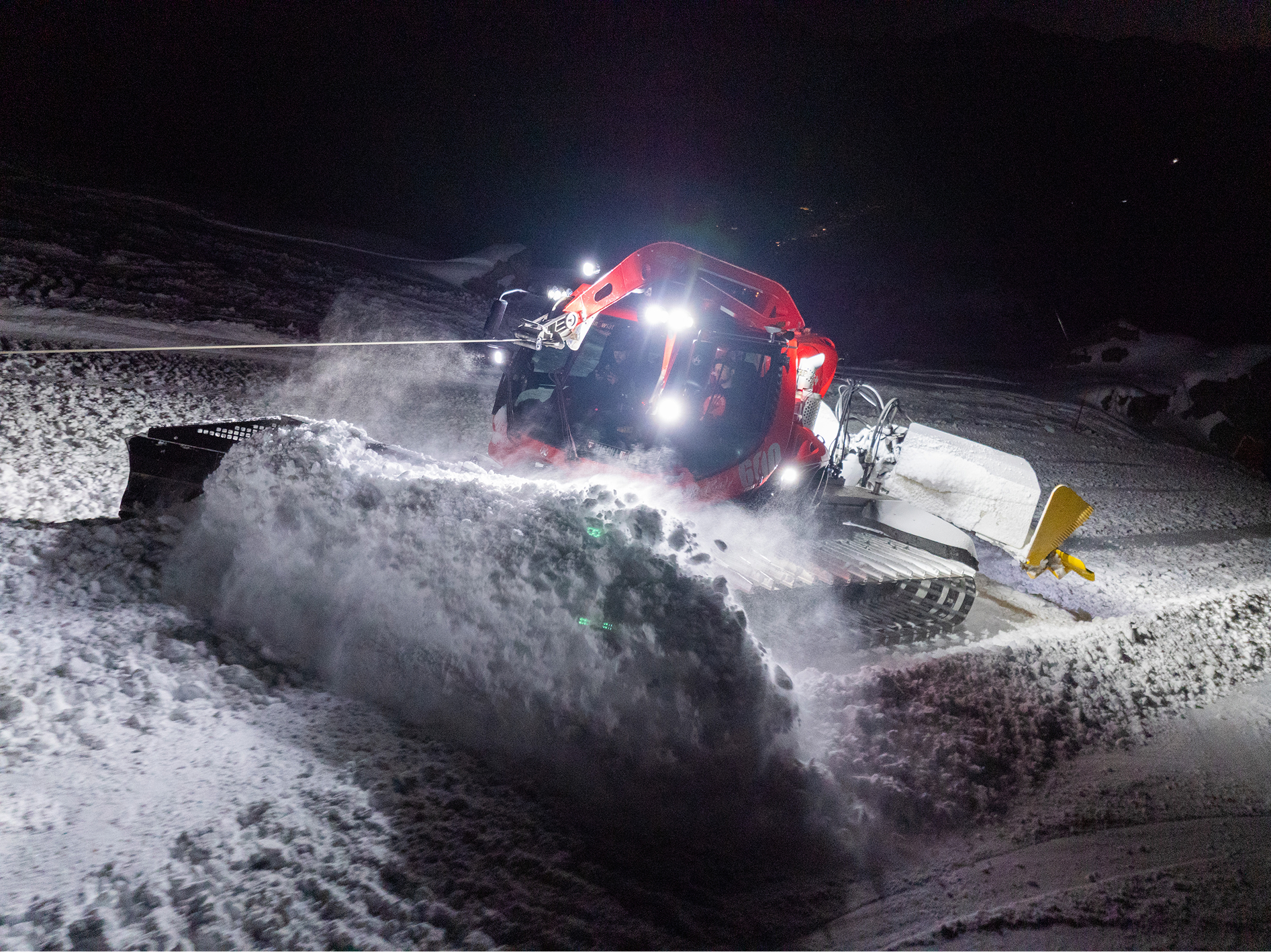 Pistenraupe schiebt bei Nacht Schnee im Scheinwerferlicht