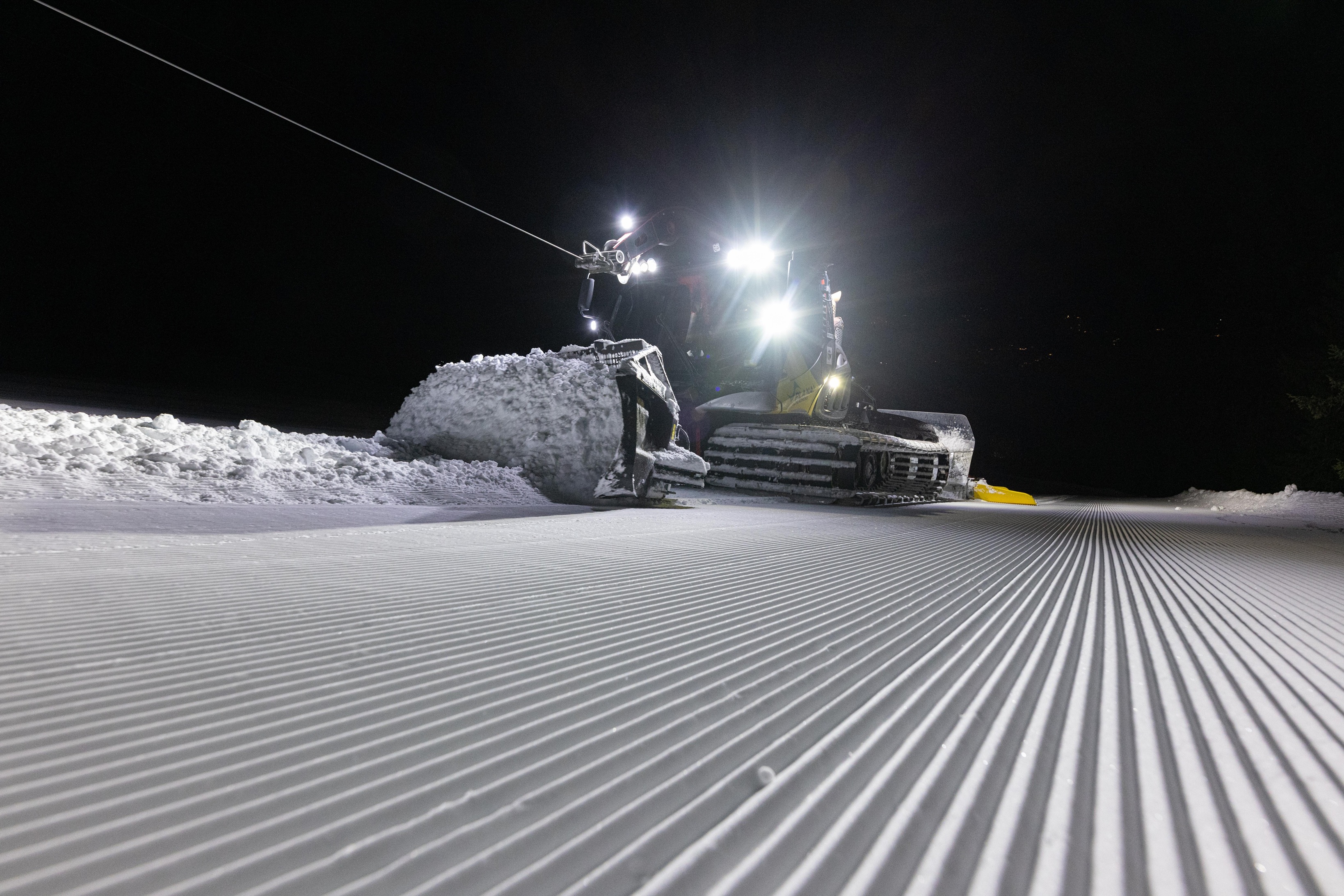 Pistenraupe bei Nacht, im Vordergrund das frische Fräsmuster der Piste