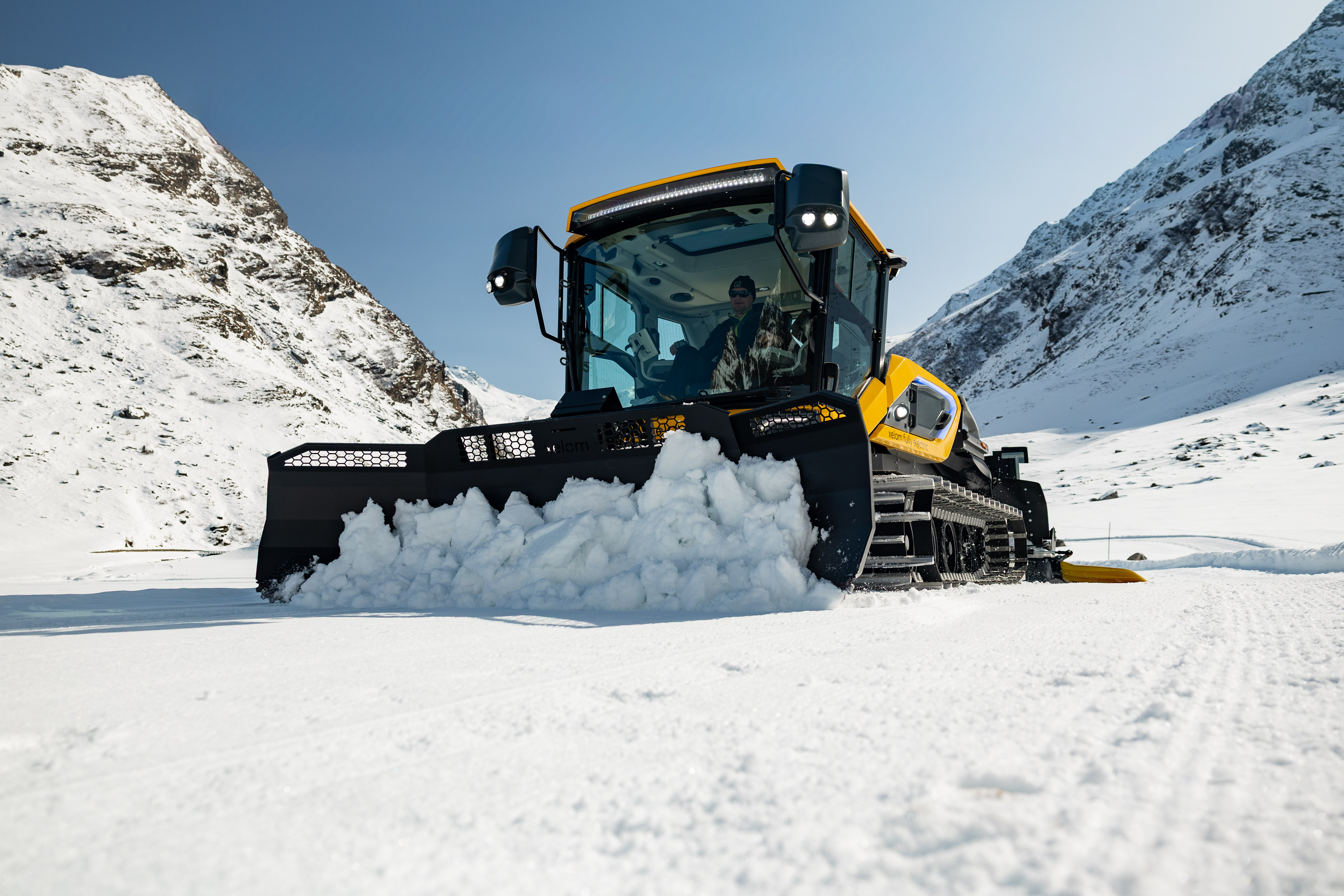 Pistenraupe mit angehobenem Schneeschild vor verschneiter Bergkulisse