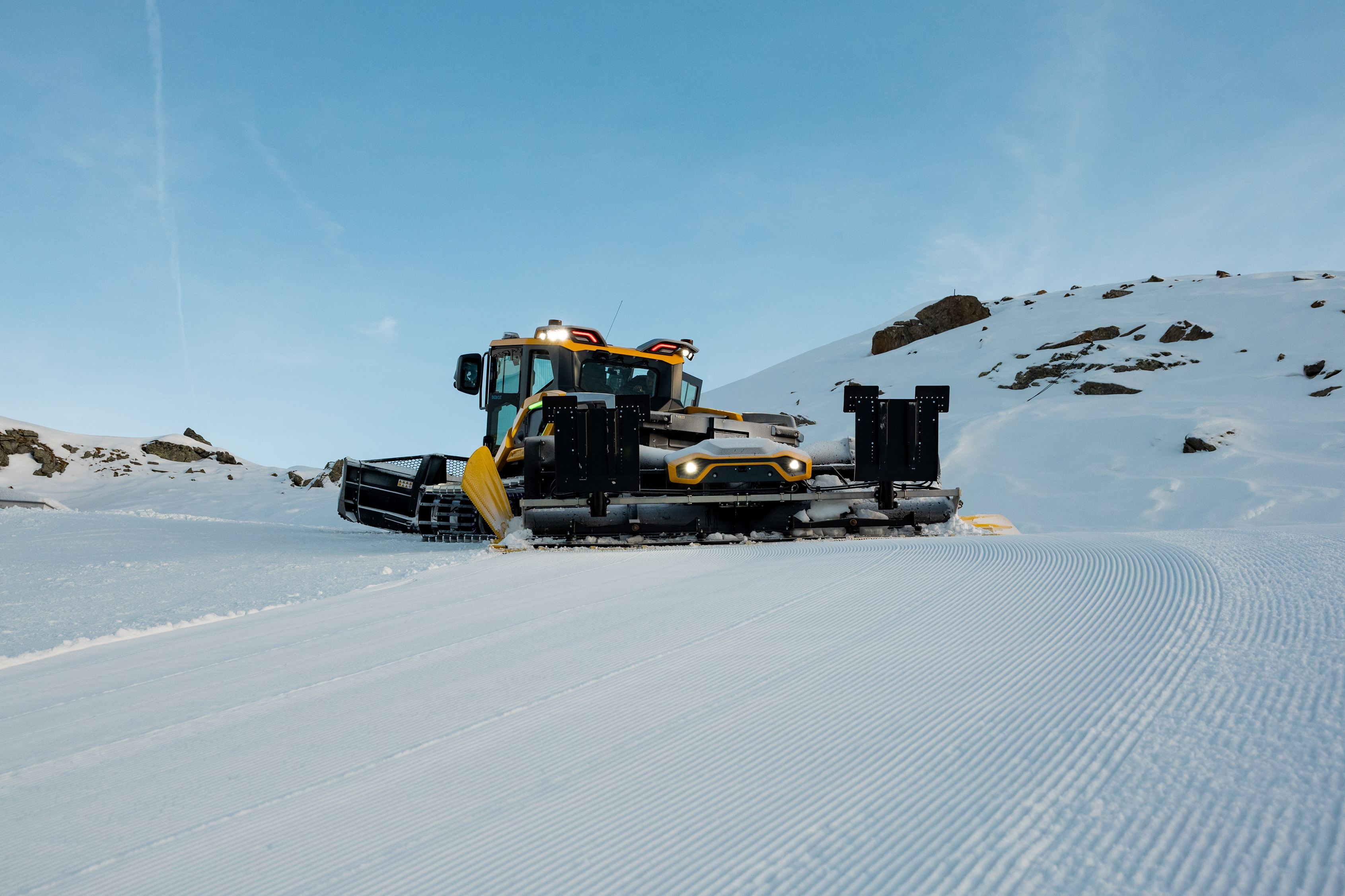 Pistenraupe auf frisch präparierter Piste vor sonnenbeschienenen Bergen