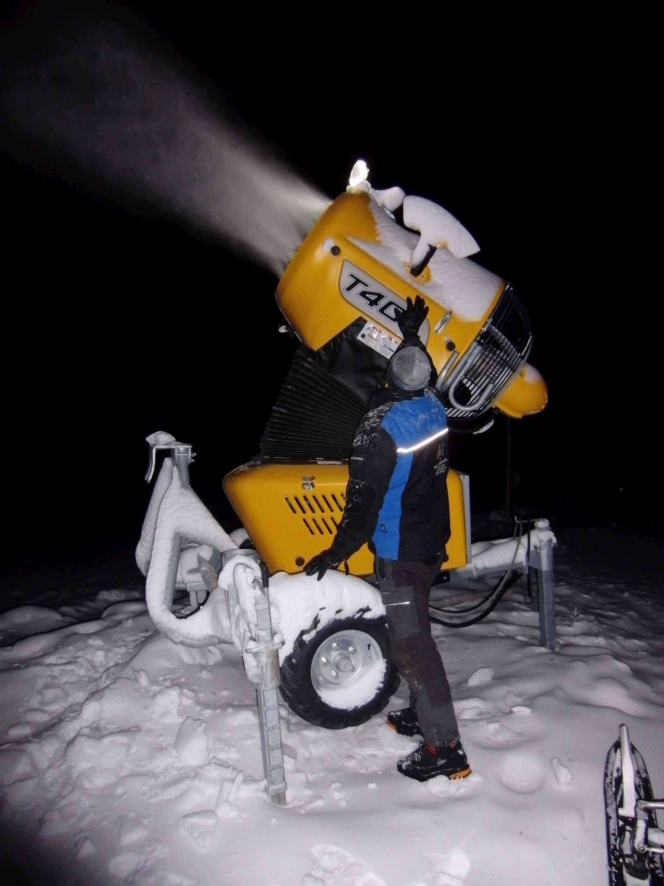 Schneekanone im nächtlichen Einsatz, daneben eine Person zur Größeneinordnung
