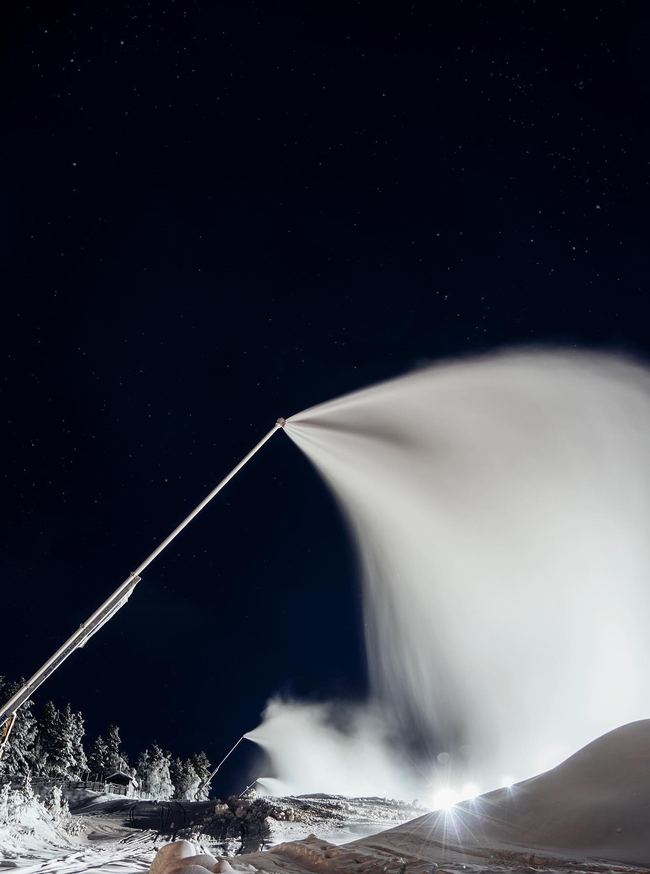Schneekanone bei Nacht mit weit reichender Schneefahne unter Sternenhimmel