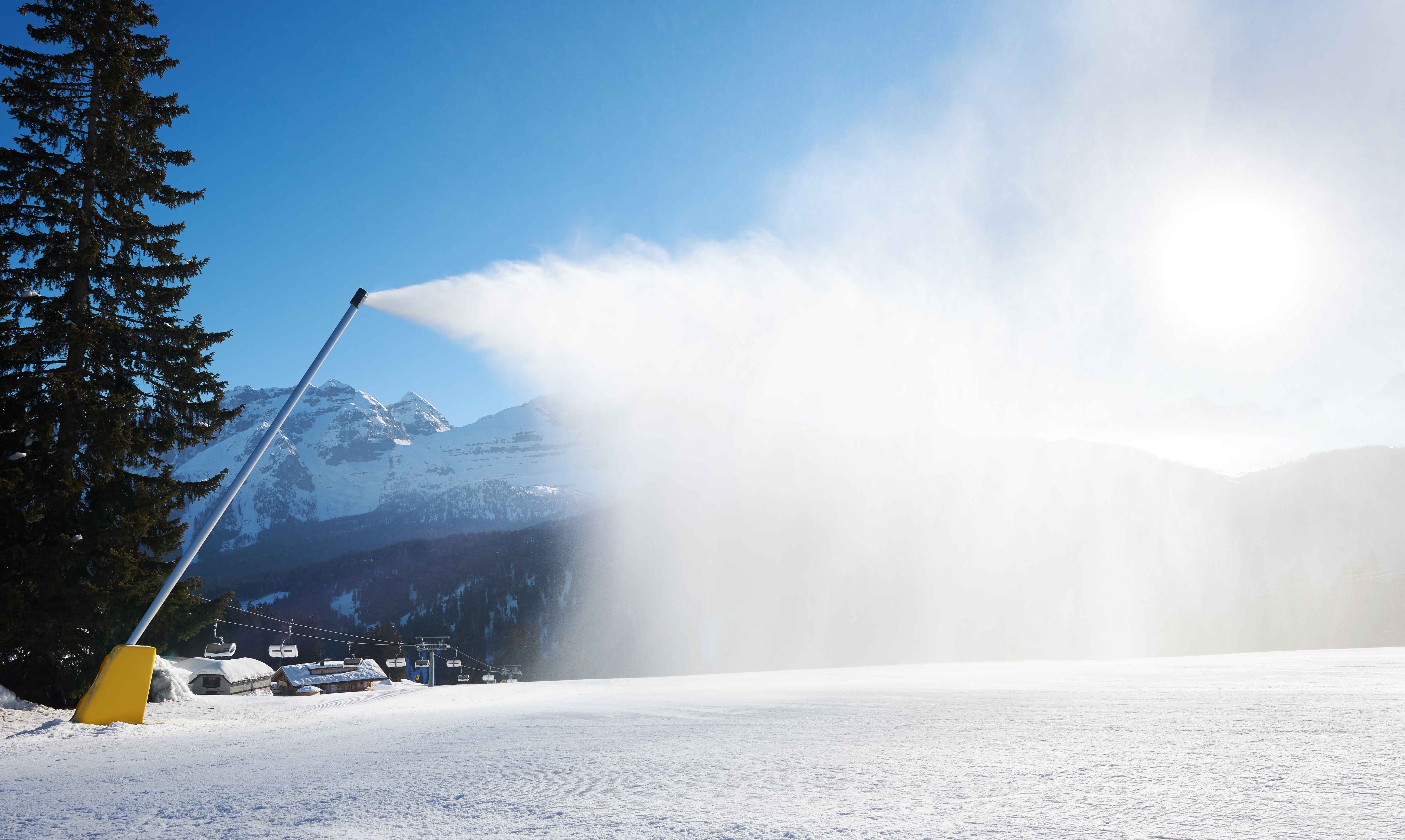 Beschneiungsanlage sprüht Schnee über eine Piste im Gegenlicht