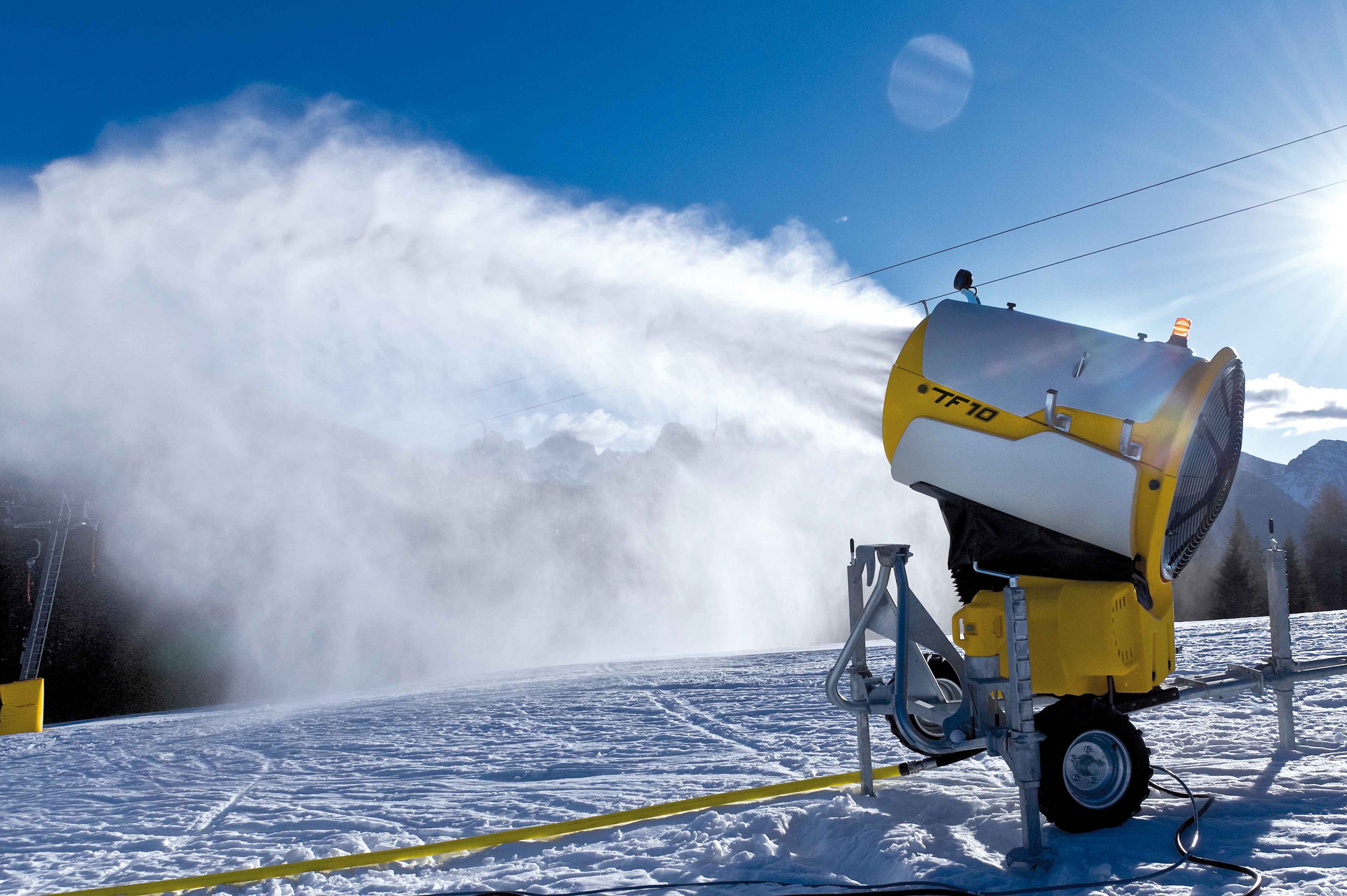 Schneekanone im Einsatz auf der Piste bei blauem Himmel