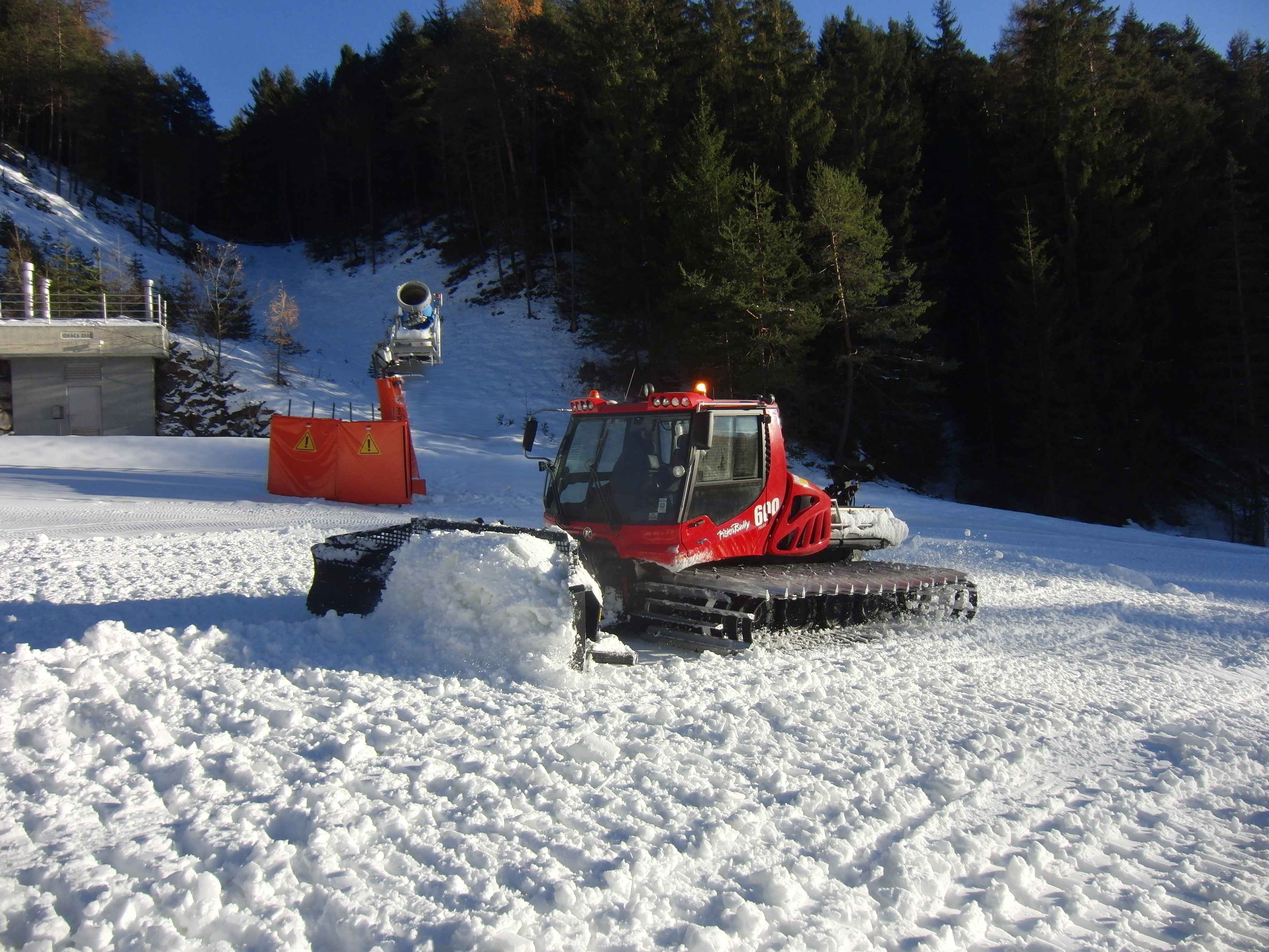 Pistenraupe mit gefülltem Schneeschild an einem Hang am Waldrand