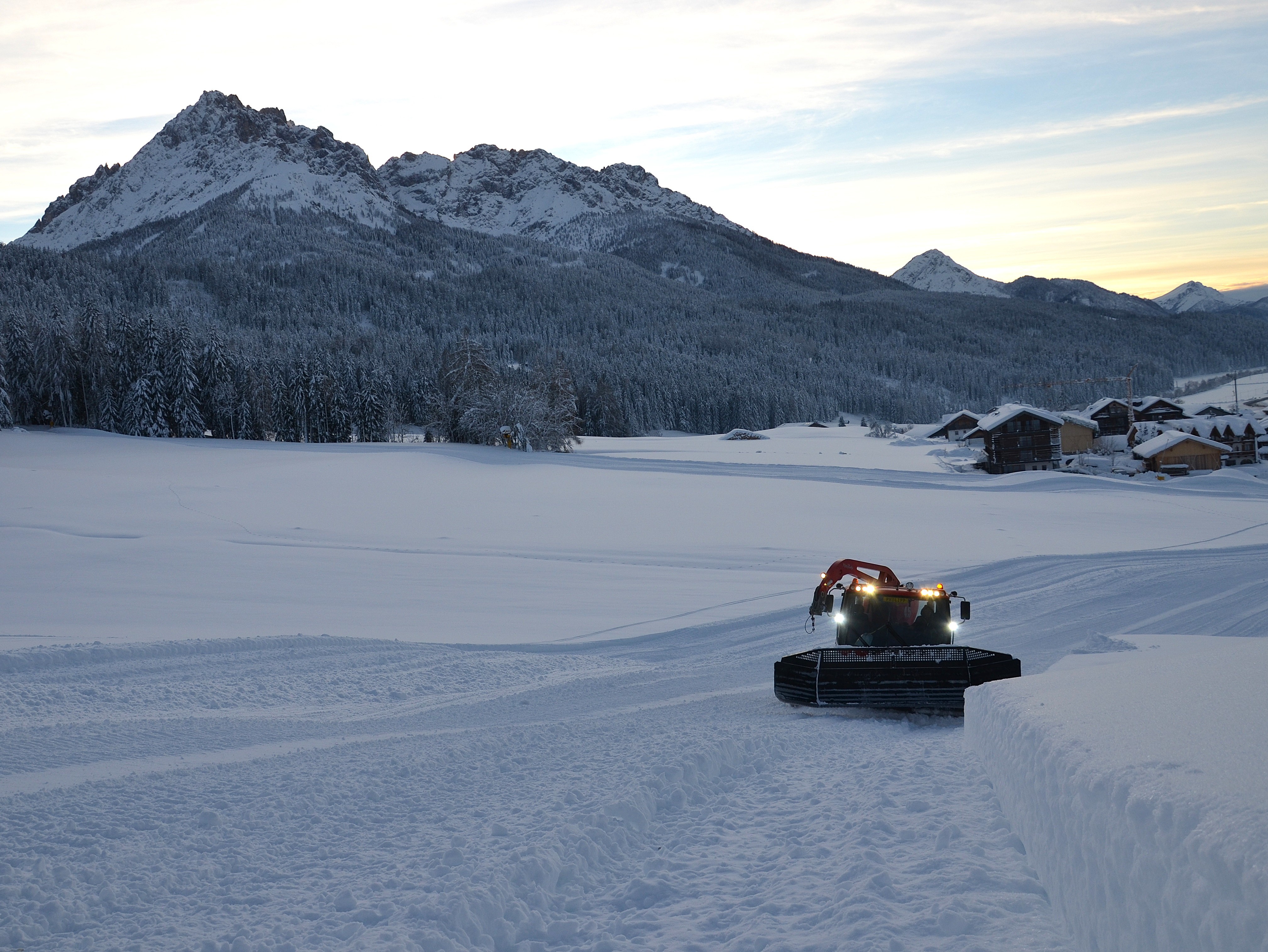 Pistenraupe auf weiter Schneefläche vor Bergkulisse im Abendlicht