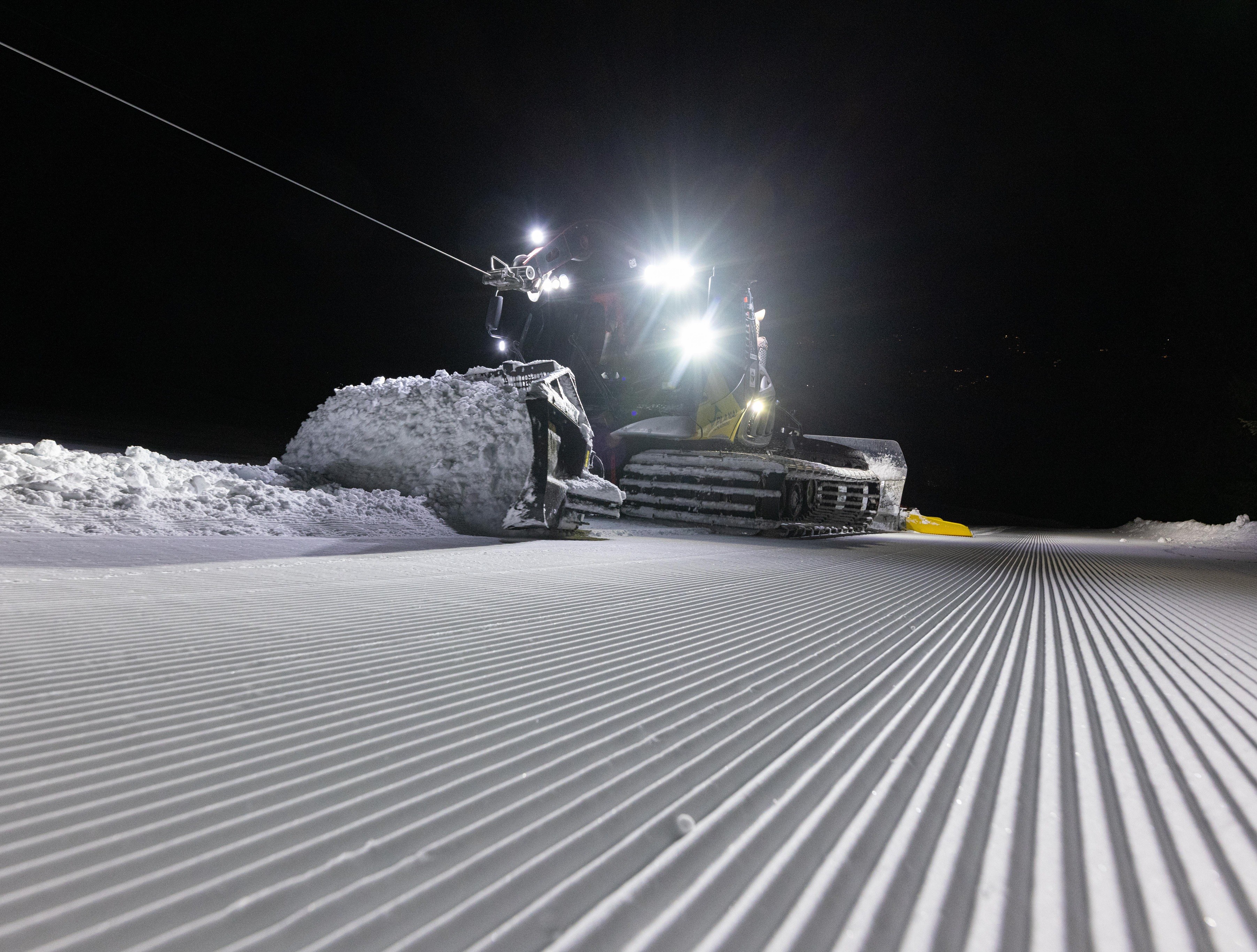 Pistenraupe bei Nacht hinter dem Fräsmuster einer frisch präparierten Piste