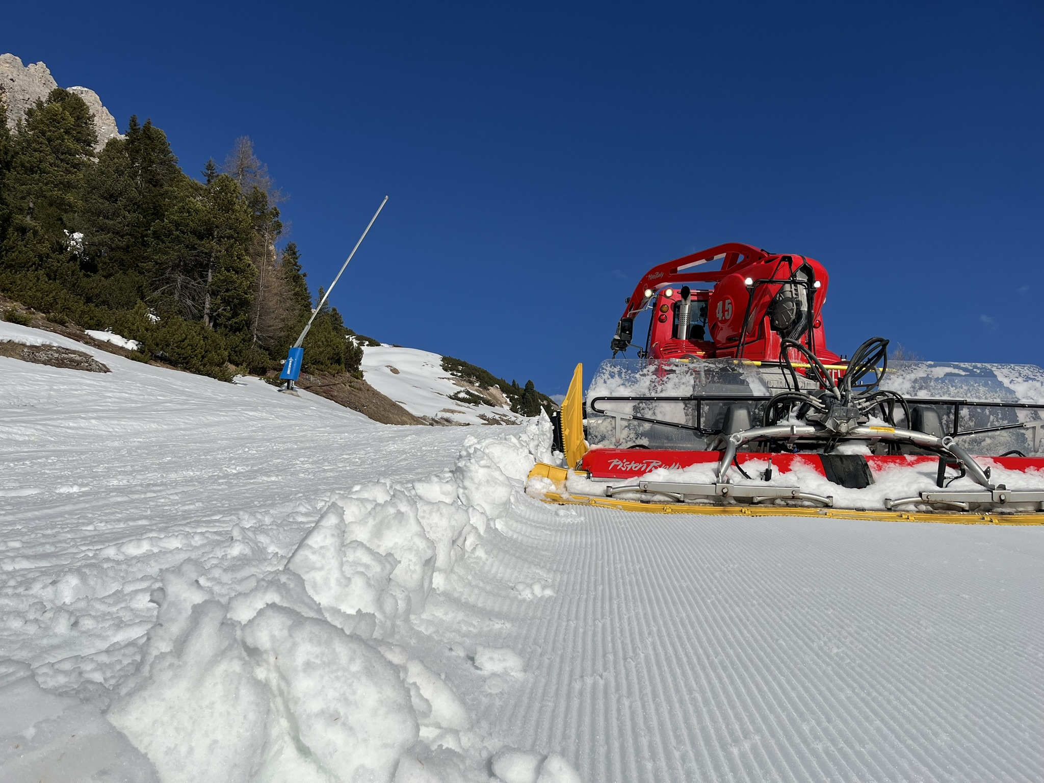 Pistenraupe frontal auf einer frisch gezogenen Piste am Waldrand