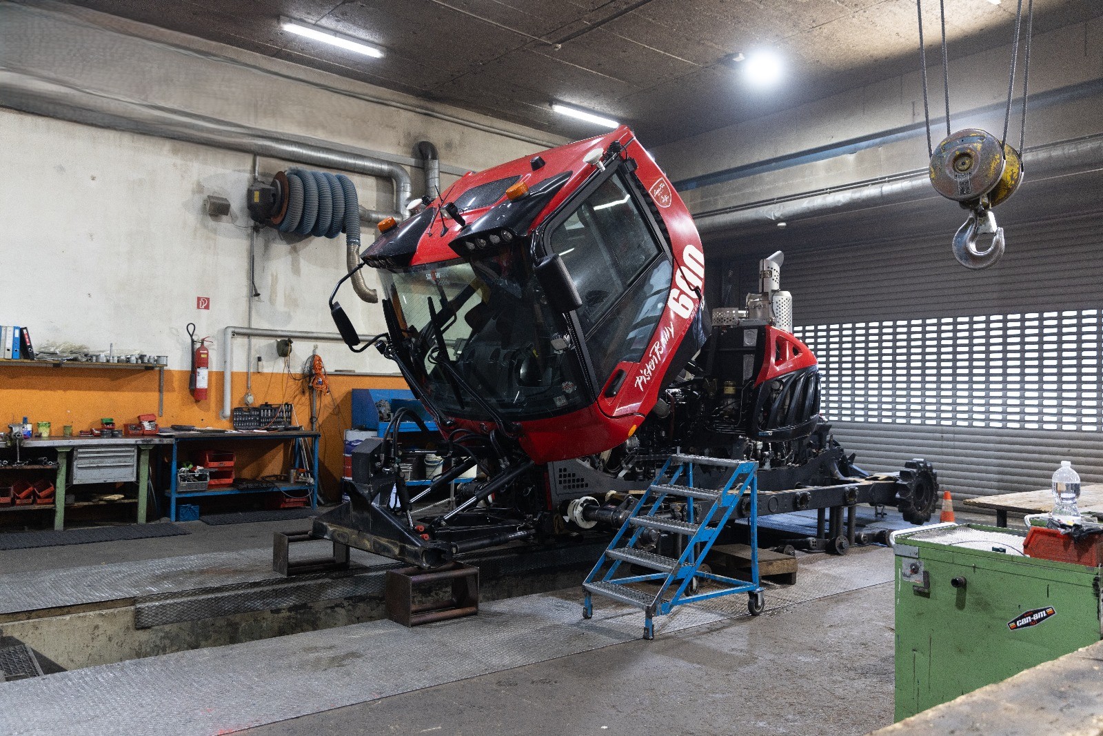 Pistenraupe mit hochgeklappter Kabine zur Wartung in der Werkstatt aufgebockt